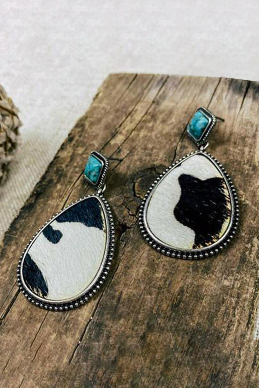 Black cow print turquoise earrings with teardrop shape and silver bead detailing on wood background
