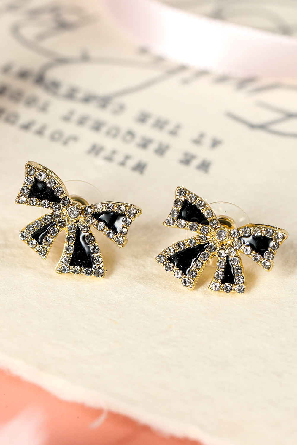kjplussizefashion black rhinestone bow earrings with gold-tone detailing on a vintage paper background