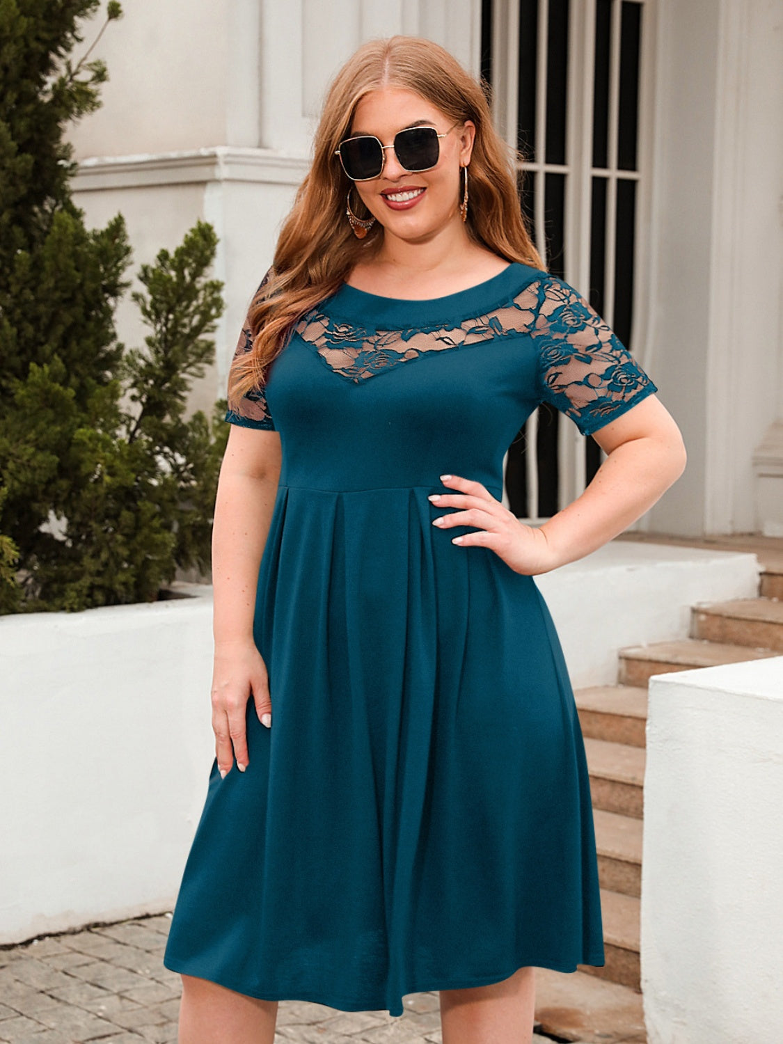 Plus size ruched round neck dress with lace short sleeves and flowy skirt in teal worn outdoors