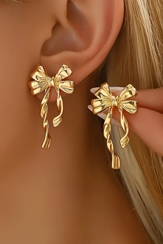 Gold bow stud earrings worn on ear and held by hand showcasing elegant bow design
