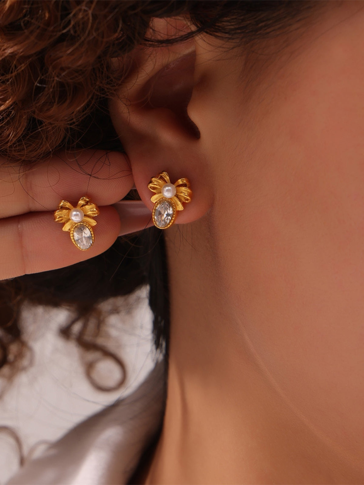Gold titanium steel bow stud earrings with pearl and crystal detail worn on ear