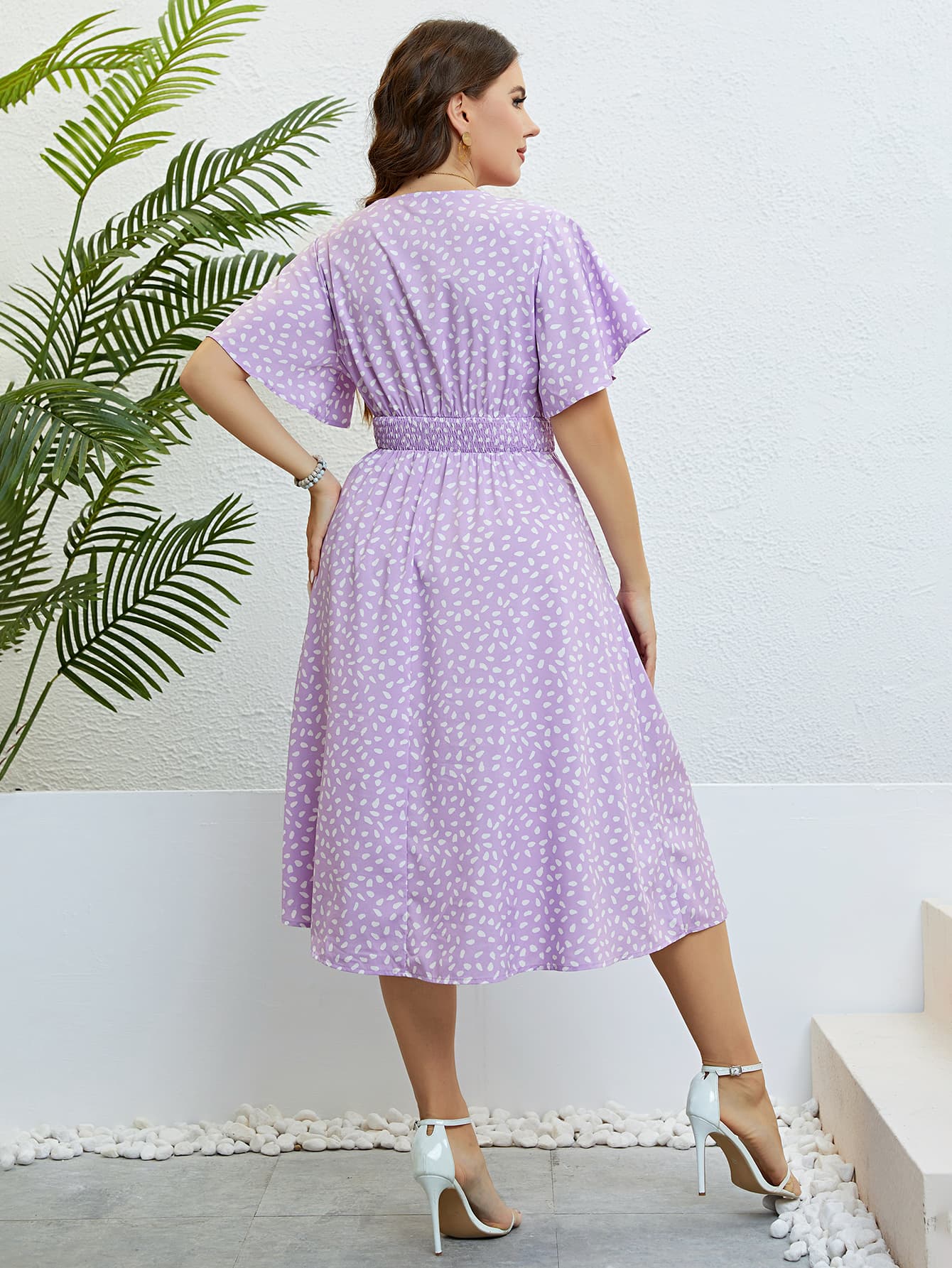 Back view of a woman wearing a lilac plus size floral smocked dress with white heels indoors