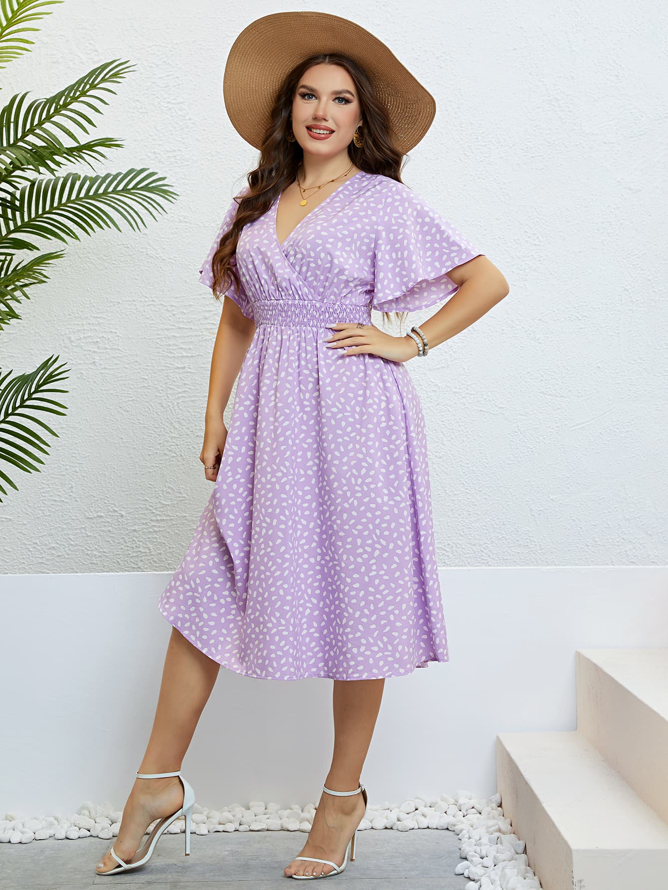 Woman wearing a plus size floral smocked dress in lavender with white patterns and a wide-brim hat