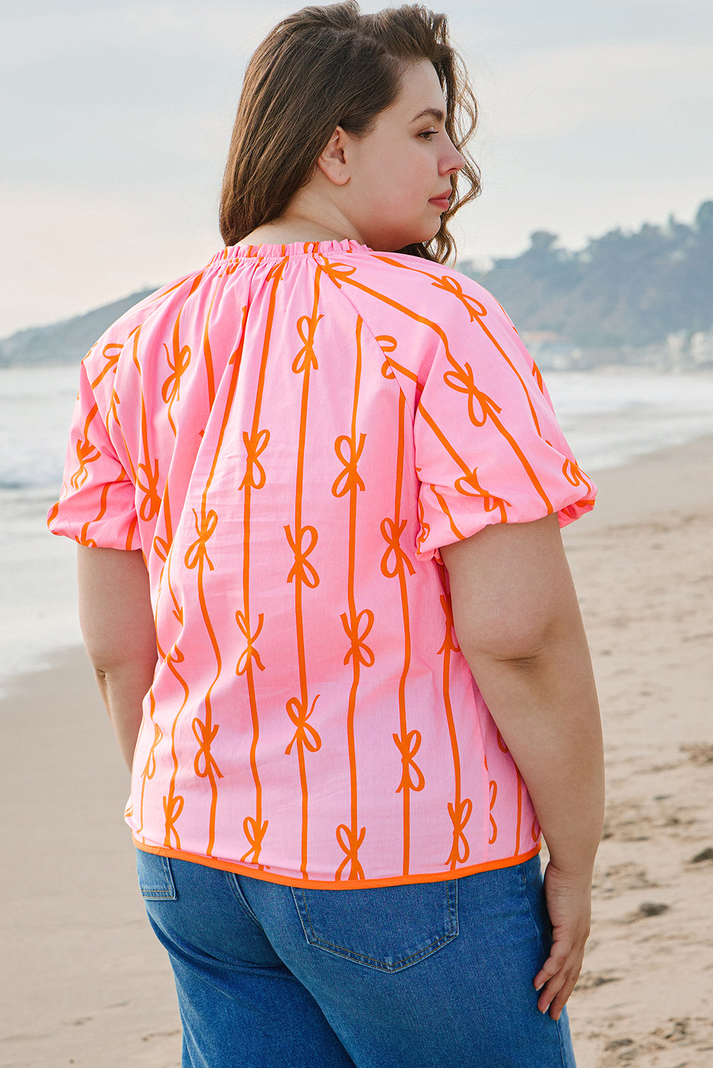 Plus size rose bowknot blouse in pink with orange bow patterns worn by a woman at the beach