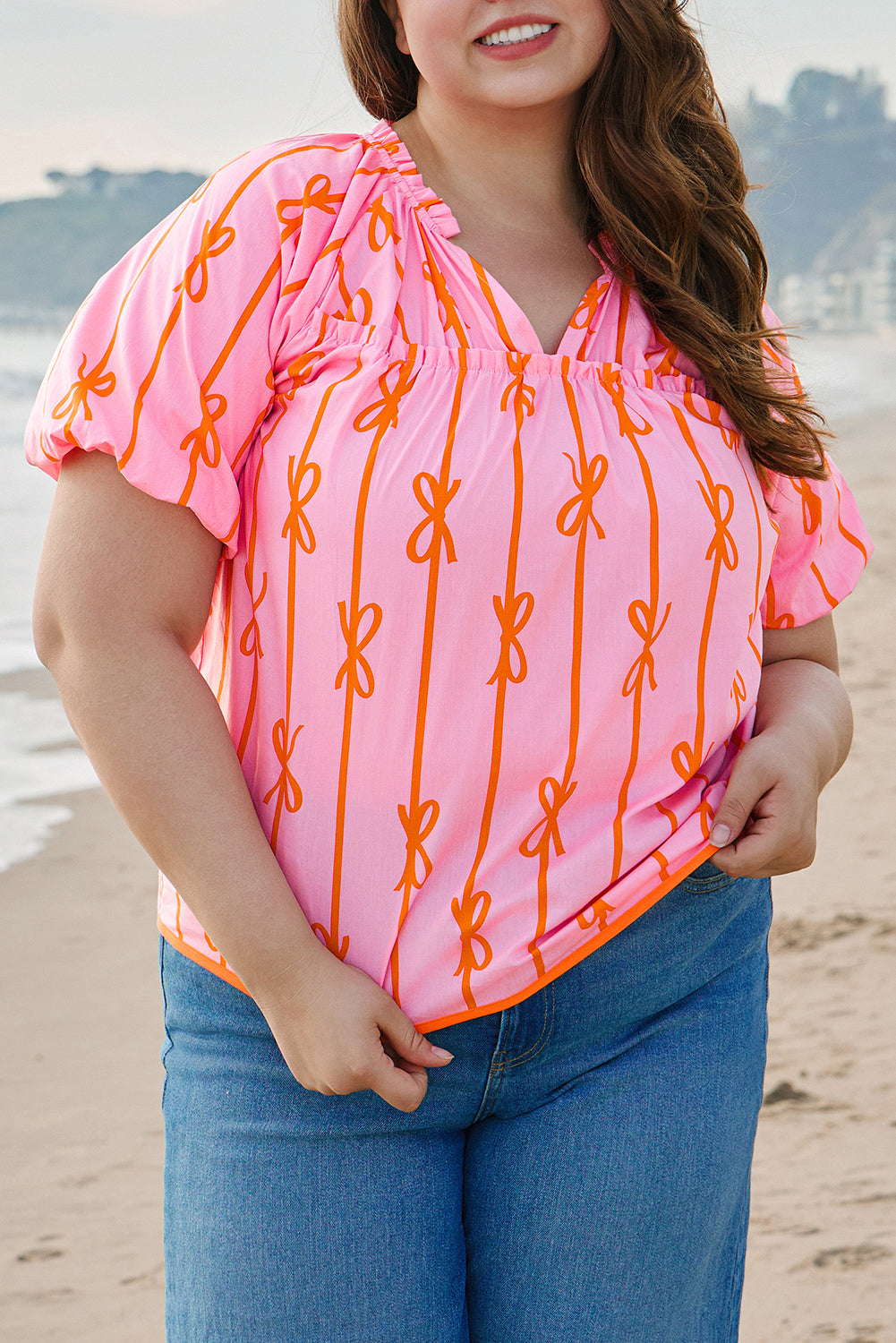 Plus size rose bowknot blouse in pink with orange bow print worn by a woman on the beach