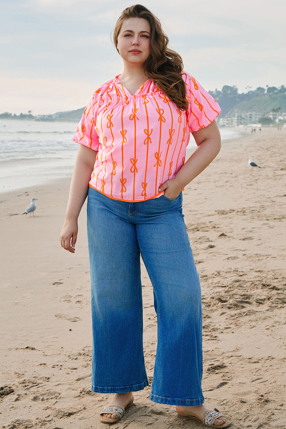 Plus size rose bowknot blouse in pink with orange bow patterns worn with blue wide-leg jeans on the beach