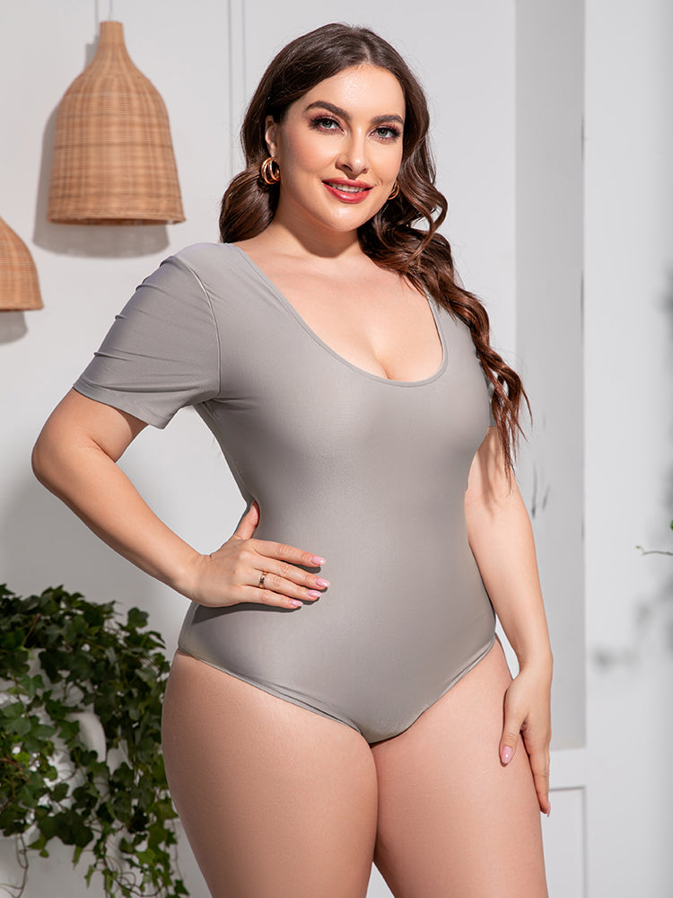 Trendsi plus size scoop neck swimsuit in light gray with short sleeves modeled by a smiling woman