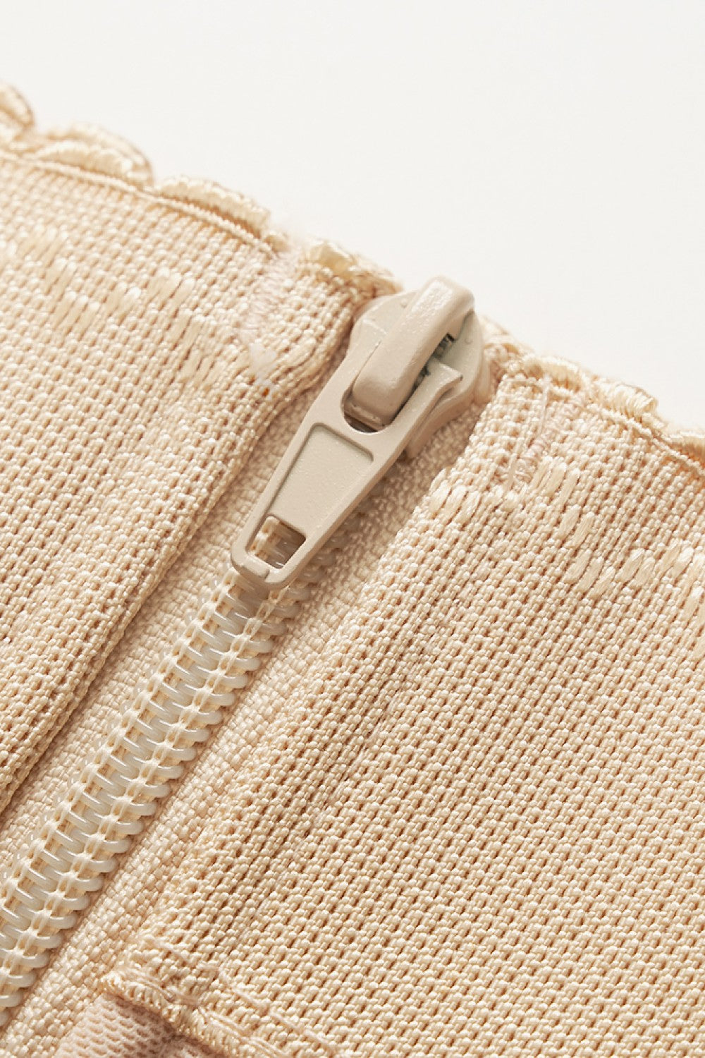 Close-up view of beige zipper on a plus size shapewear bodysuit by Trendsi