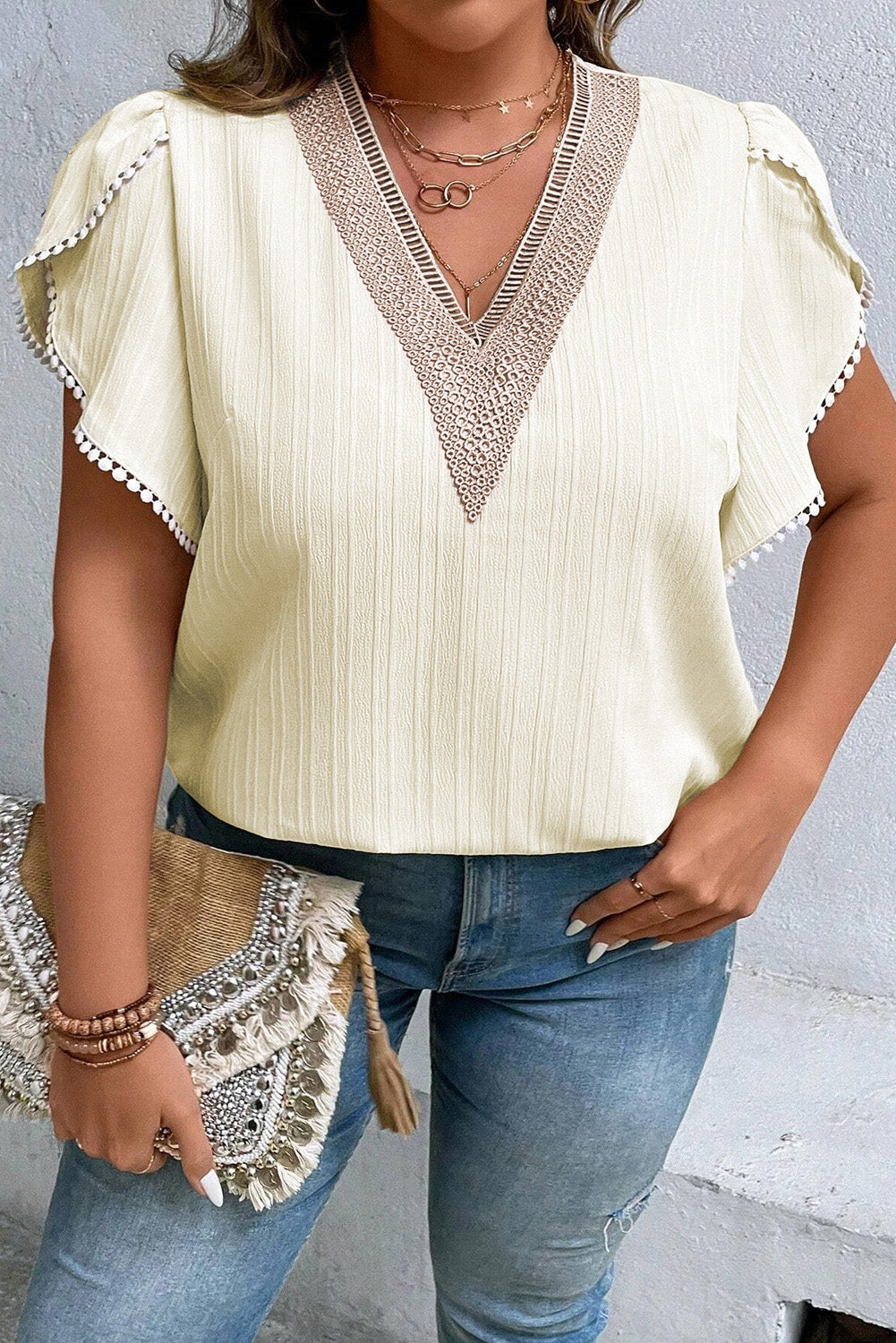 Plus size v-neck blouse with petal sleeves and decorative trim in soft cream color paired with jeans