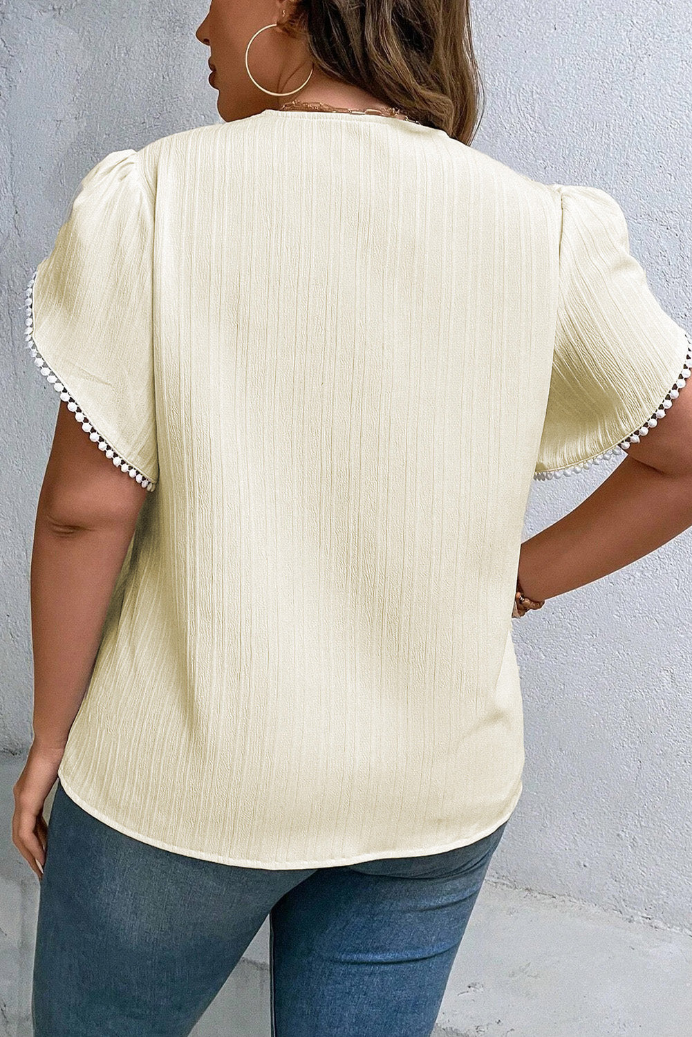 Plus size cream v-neck blouse with petal sleeves and decorative trim, relaxed fit, breathable fabric, styled with jeans