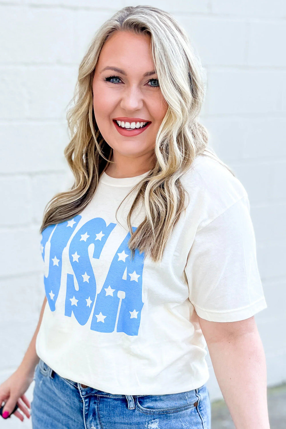 Plus size woman wearing sky blue USA graphic plus size tee paired with blue jeans smiling outdoors