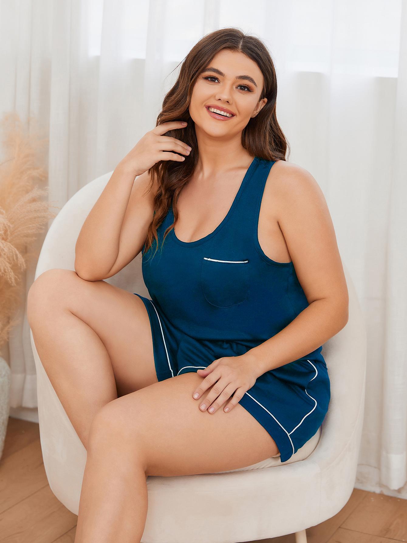 Curvy woman wearing trendy plus size sleepwear for women in navy blue sitting on white chair