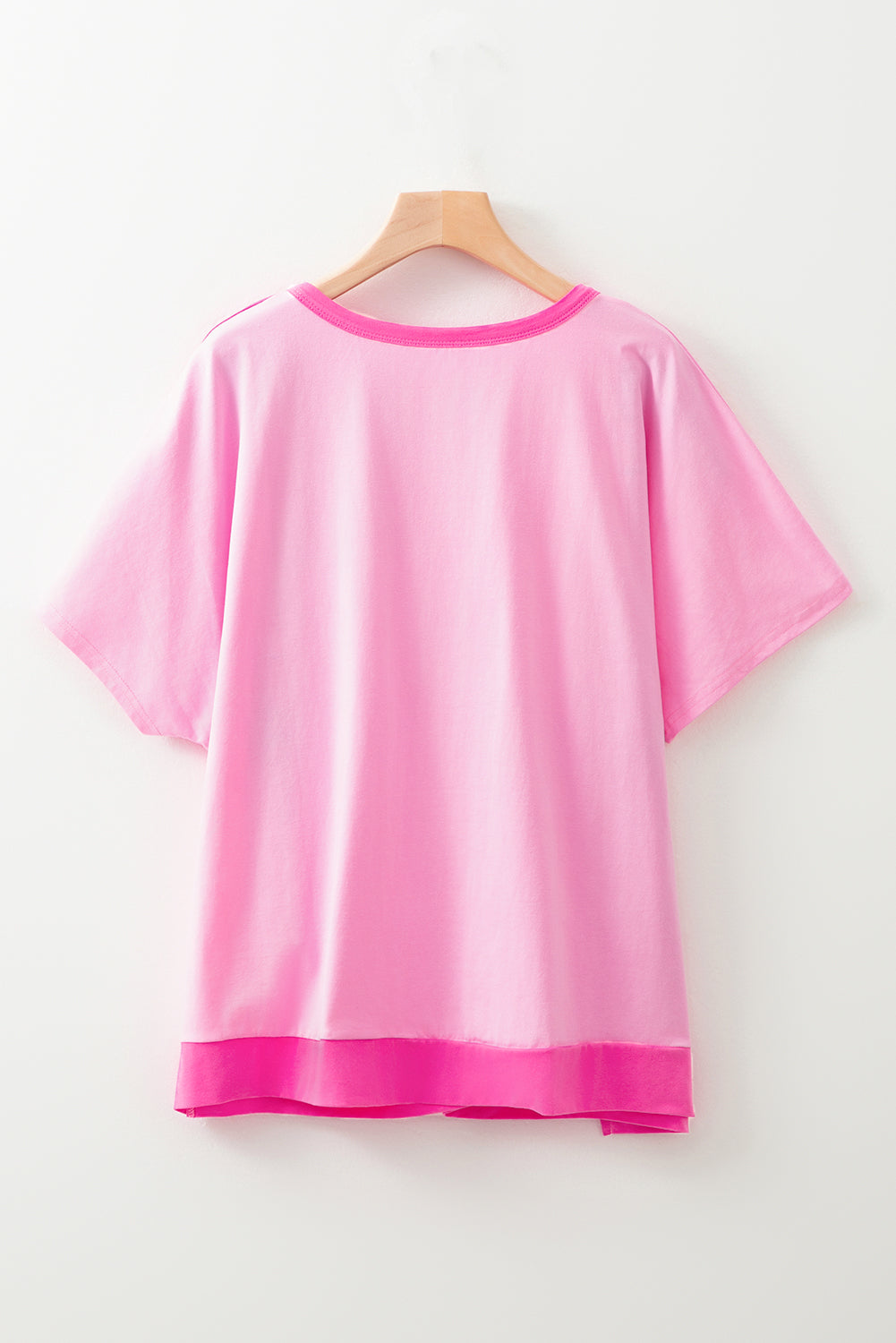 Bright pink short sleeve top for curvy women hanging on wooden hanger with contrast hem and neckline
