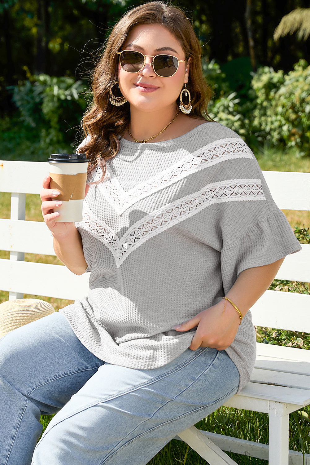 Plus size model wearing light grey ruffle sleeve blouse with lace details sitting on bench outdoors