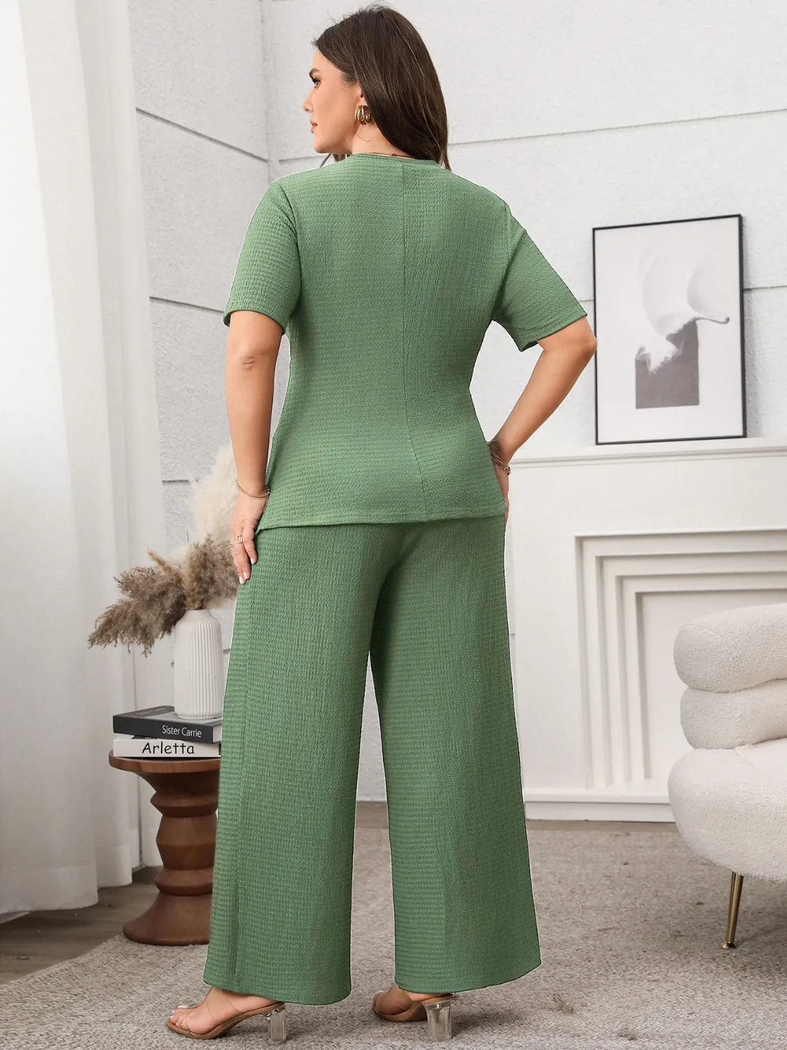 Plus size asymmetrical pants set in green textured fabric worn by woman standing indoors