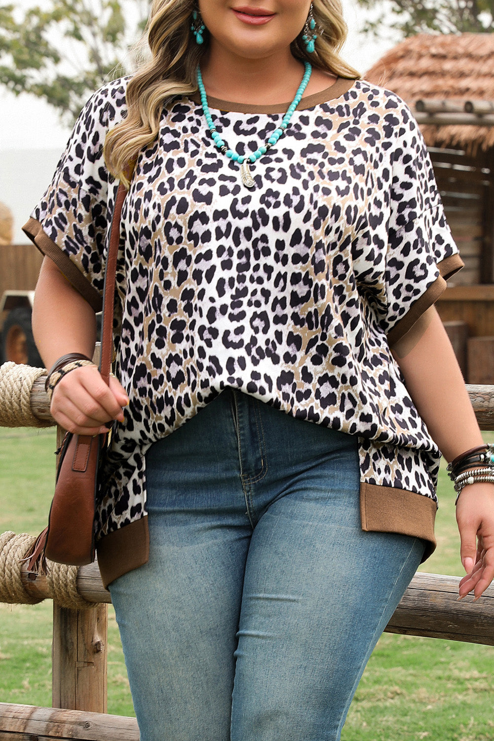 Plus size leopard print top with short sleeves and brown trim worn with blue jeans outdoors