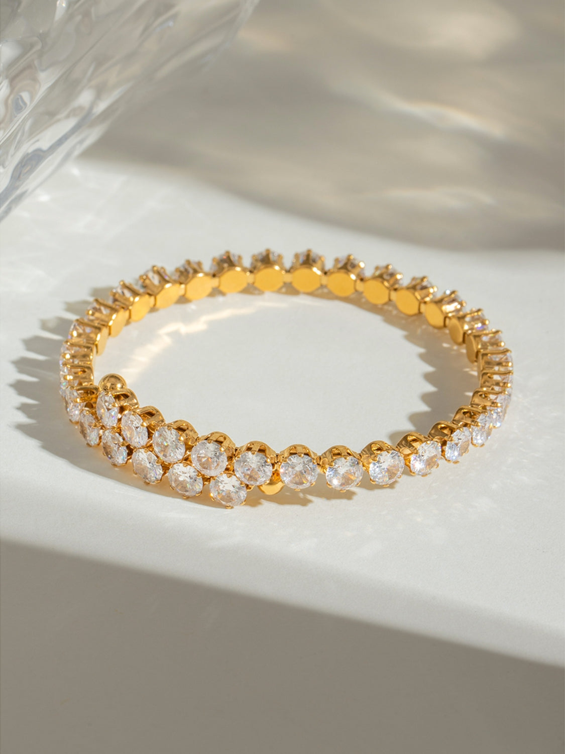 Gold stainless steel zircon bracelet with sparkling round stones on a light surface