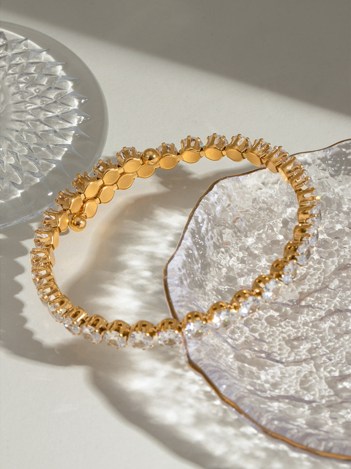 Elegant gold-toned stainless steel zircon bracelet with clear sparkling stones on a textured glass surface