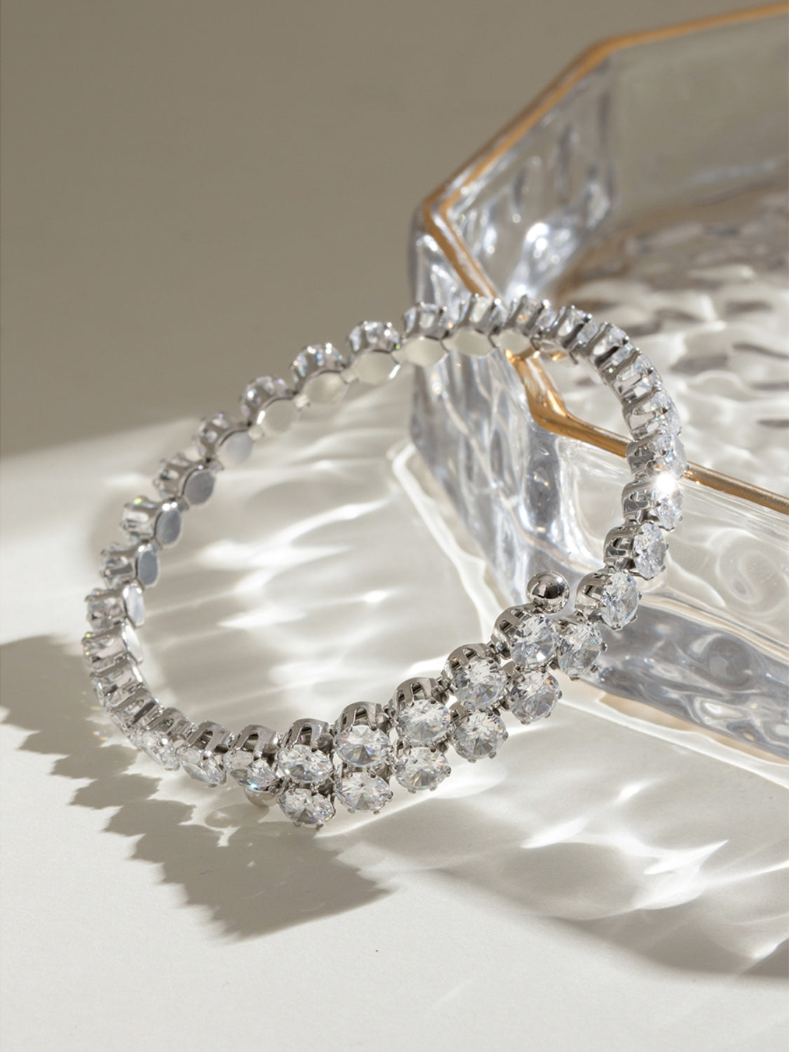 Elegant stainless steel zircon bracelet with sparkling clear stones displayed on a glass dish