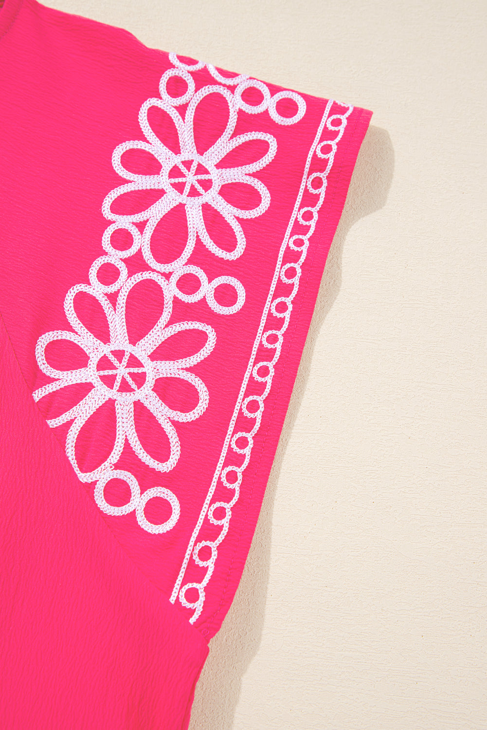 Close-up of strawberry pink embroidered blouse sleeve with white floral embroidery detail