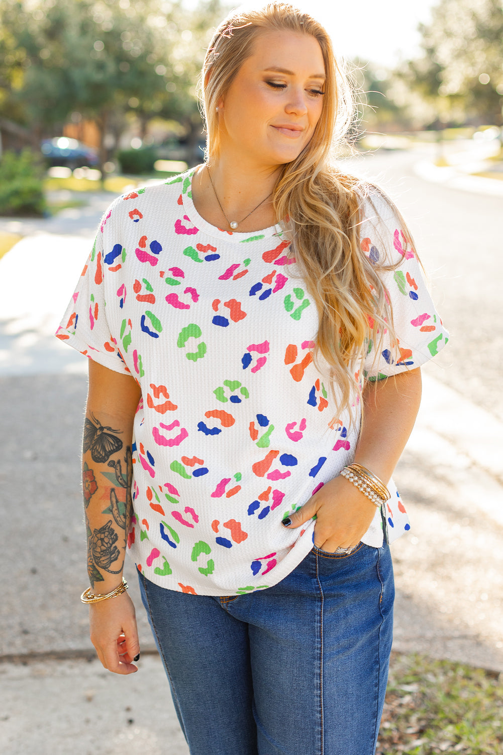 Plus size model wearing a white multicolor leopard top for women paired with blue jeans outdoors