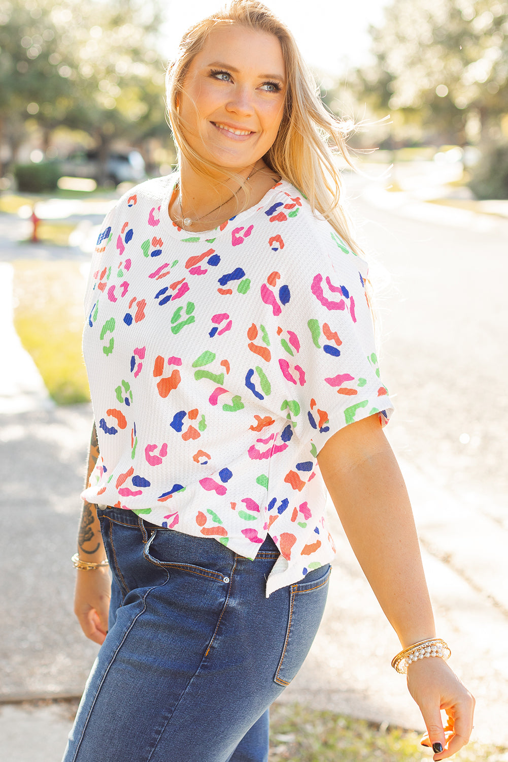 Plus size woman wearing white multicolor leopard top for women paired with blue jeans outdoors