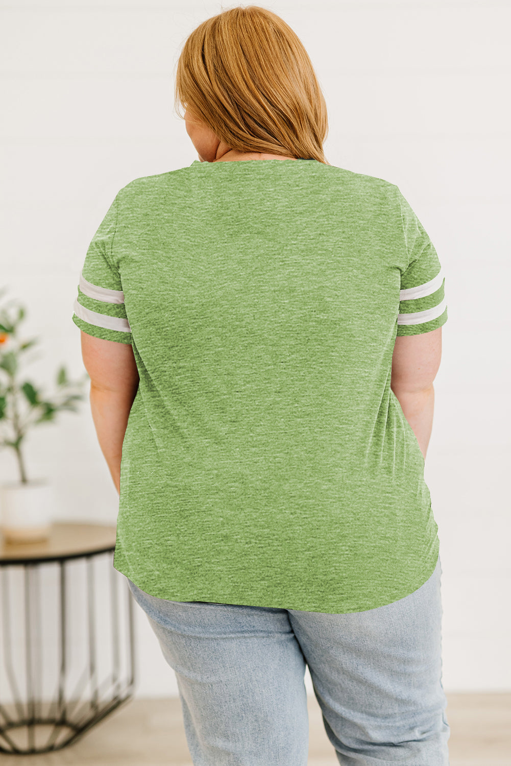 Back view of women's plus size striped sleeve top in green worn with light wash jeans