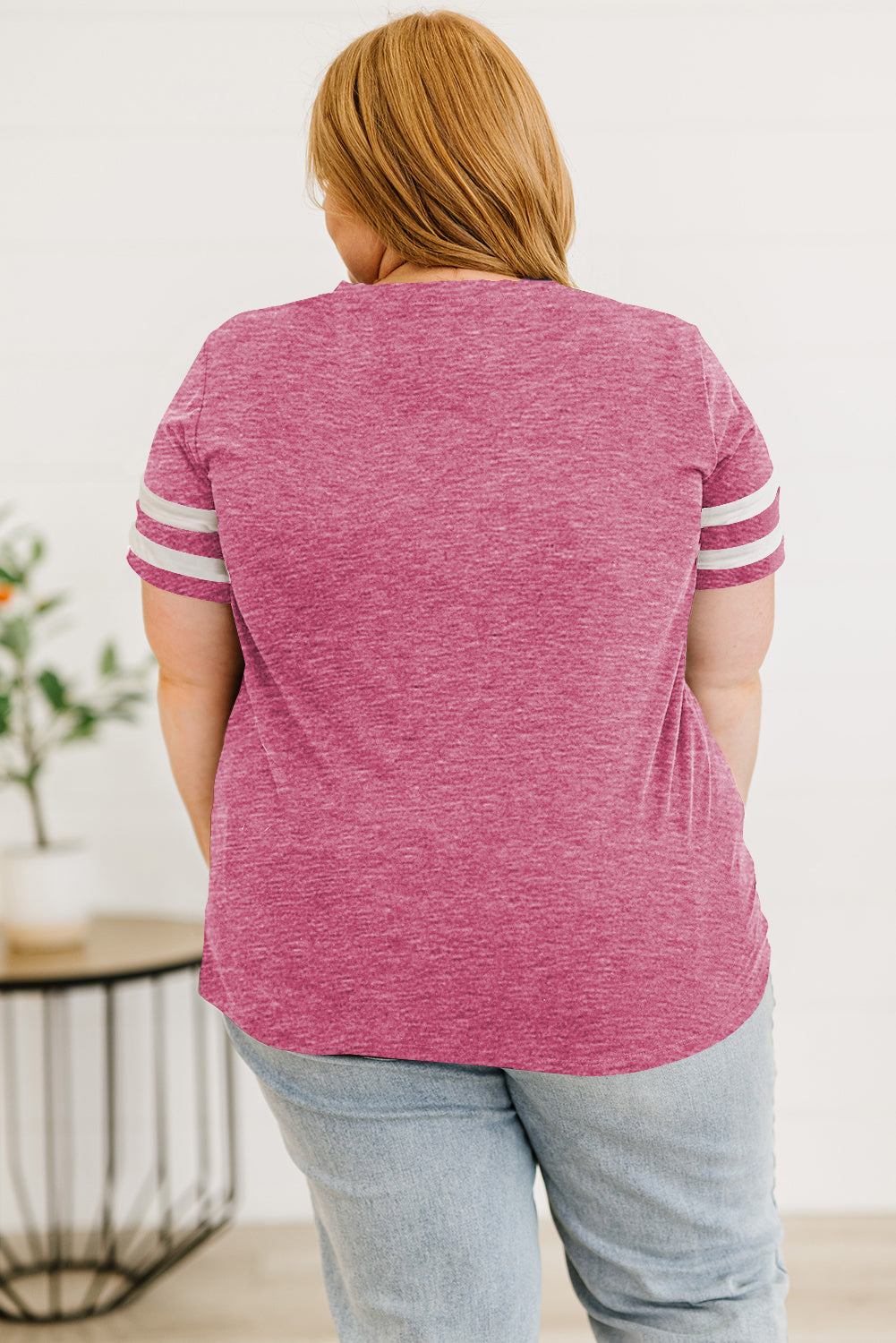 Back view of a woman wearing a women's plus size striped sleeve top in pink with white stripes and light wash jeans