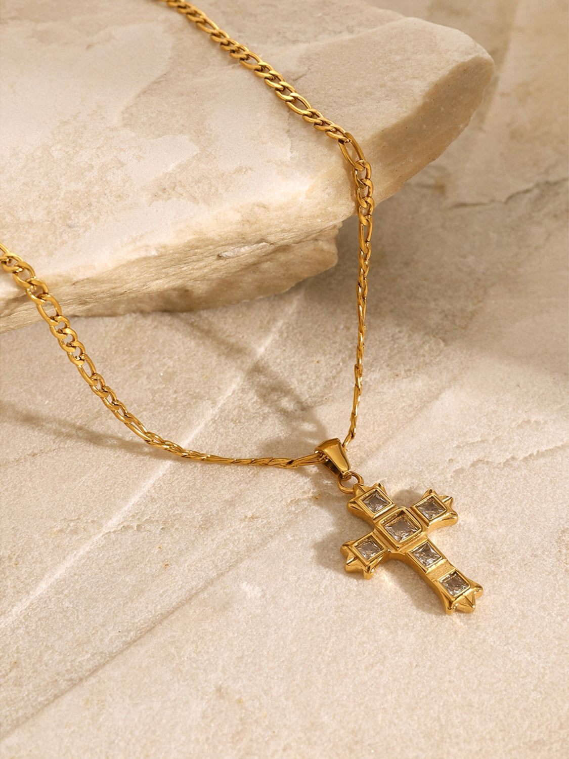 Gold chain necklace with zircon cross pendant for women displayed on a stone surface