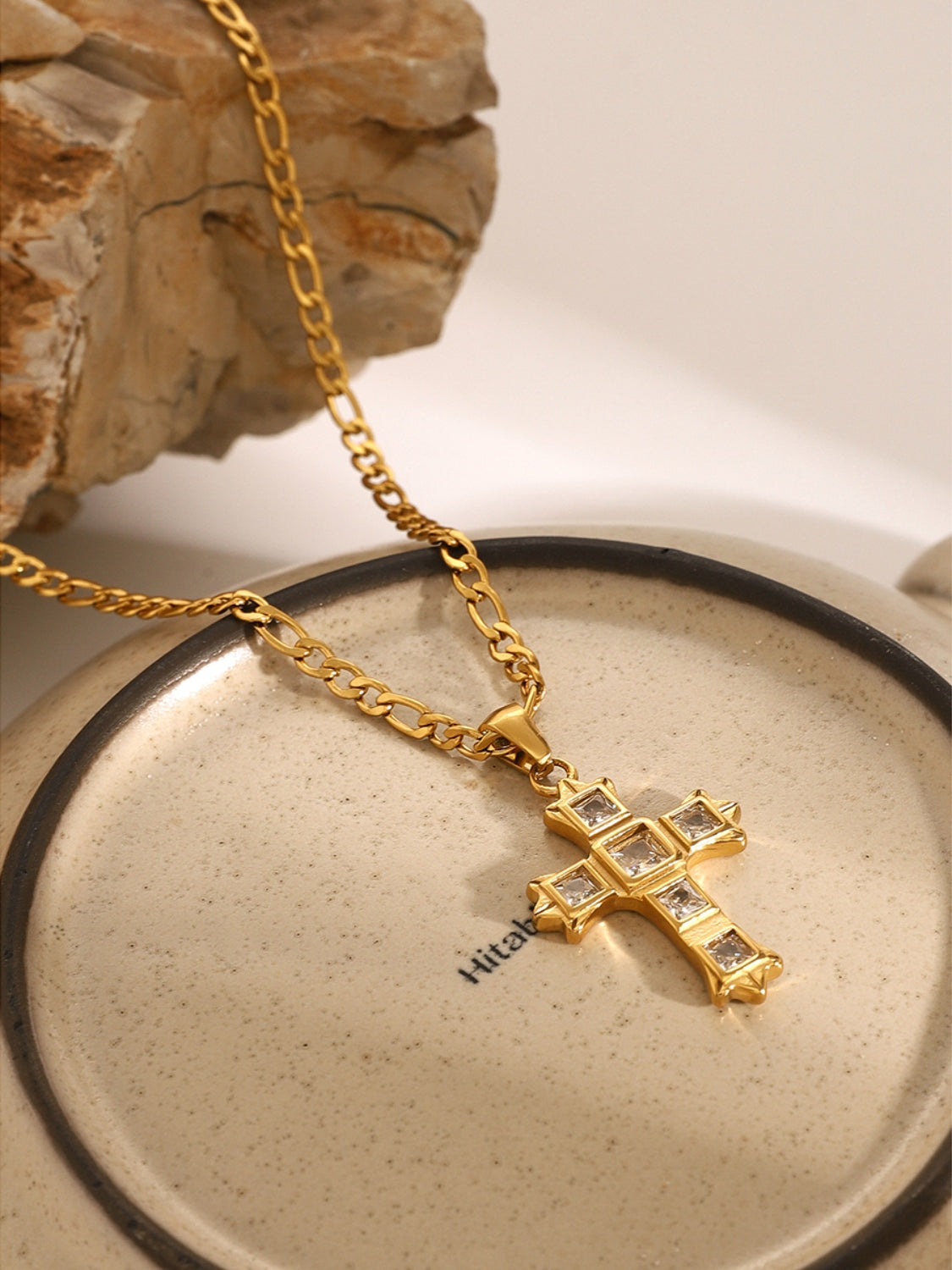 Gold zircon cross pendant for women on a matching chain displayed on a ceramic plate