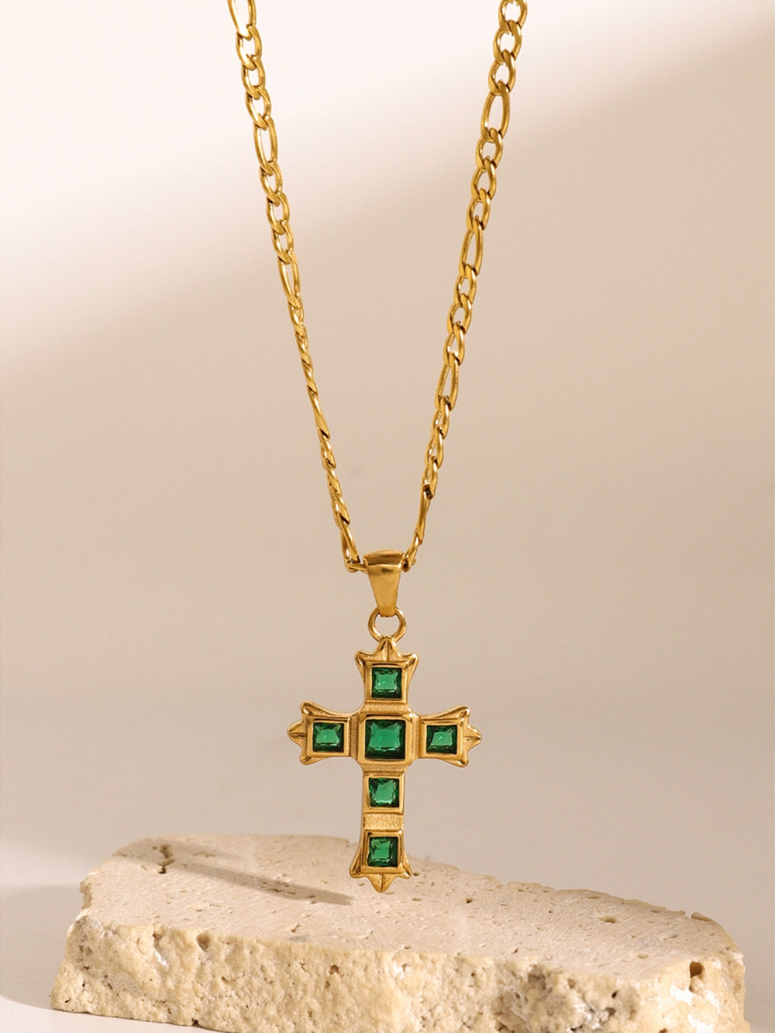 Gold chain necklace with a green zircon cross pendant for women displayed on a textured stone