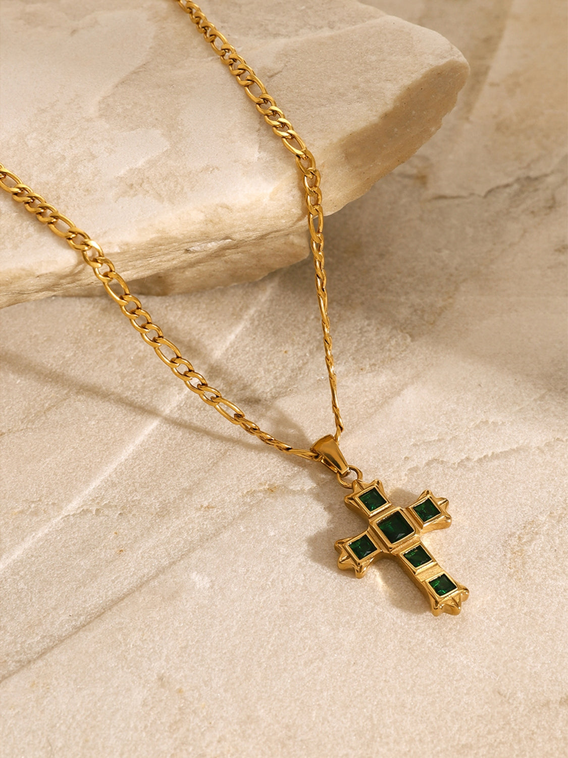 Gold chain necklace with green zircon cross pendant for women displayed on beige stone surface