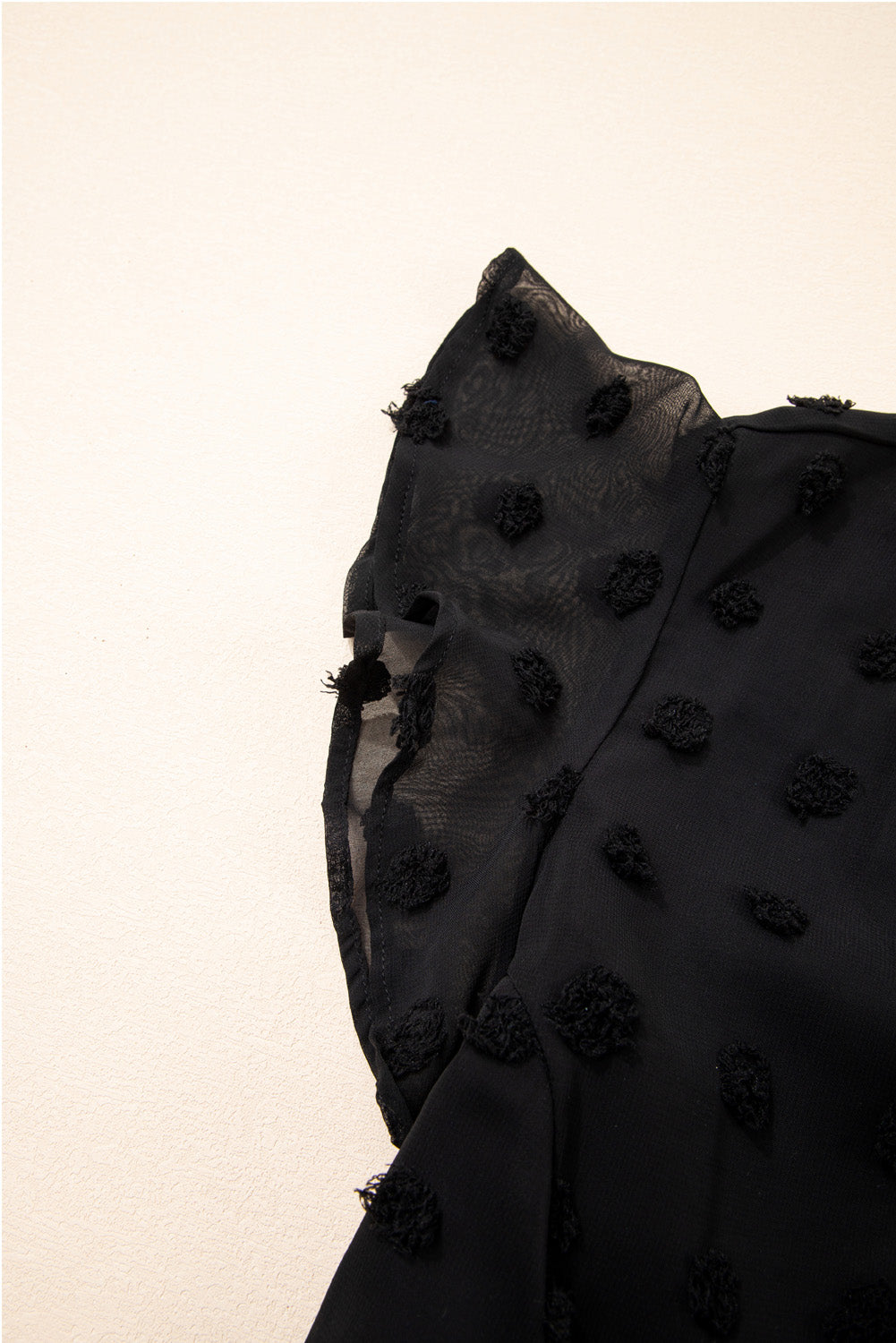 Close-up of black dotty plus size summer dress fabric with textured dot details on sheer sleeves