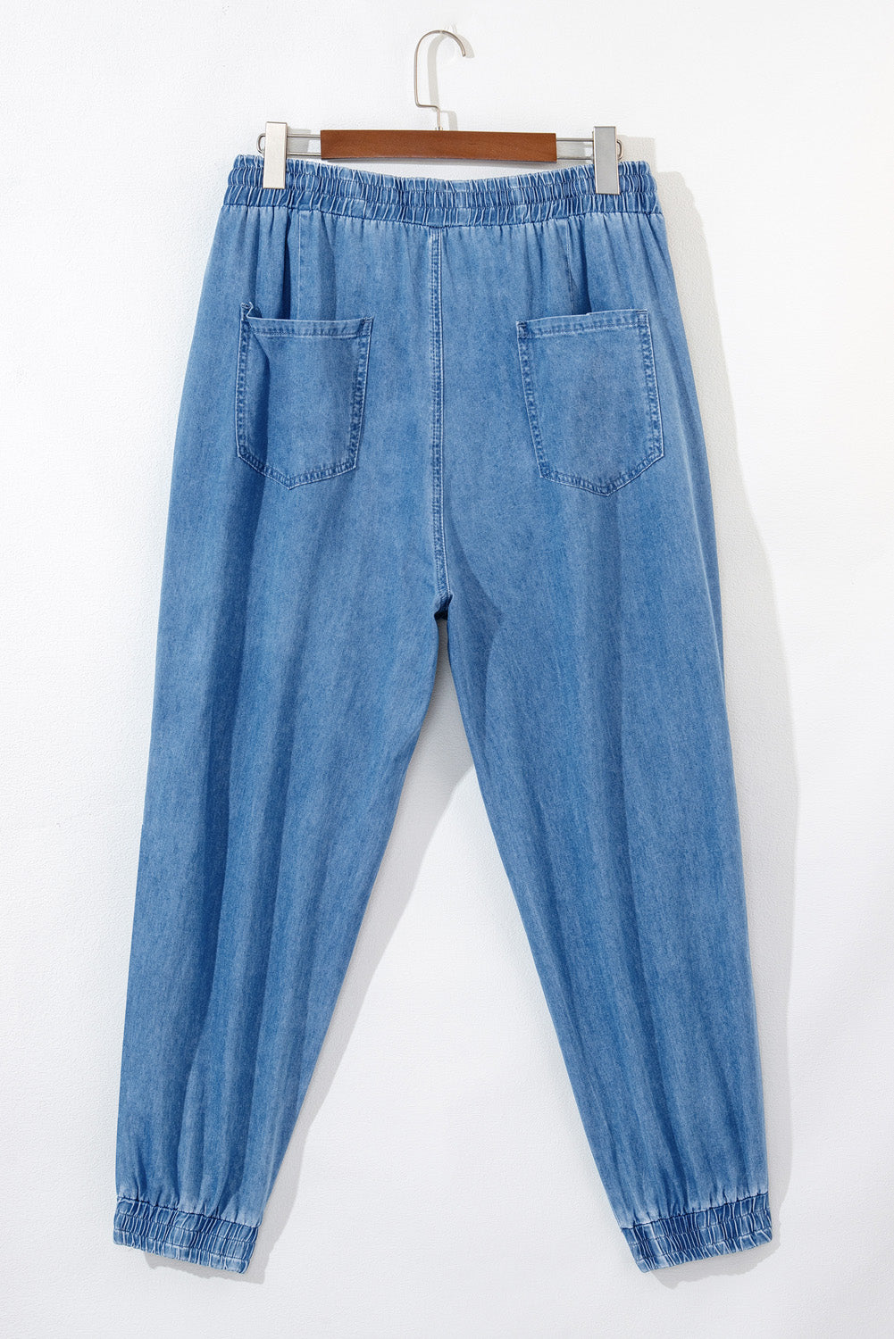 Light blue drawstring waist plus size jeans with back pockets and elastic cuffs hanging on wooden hanger