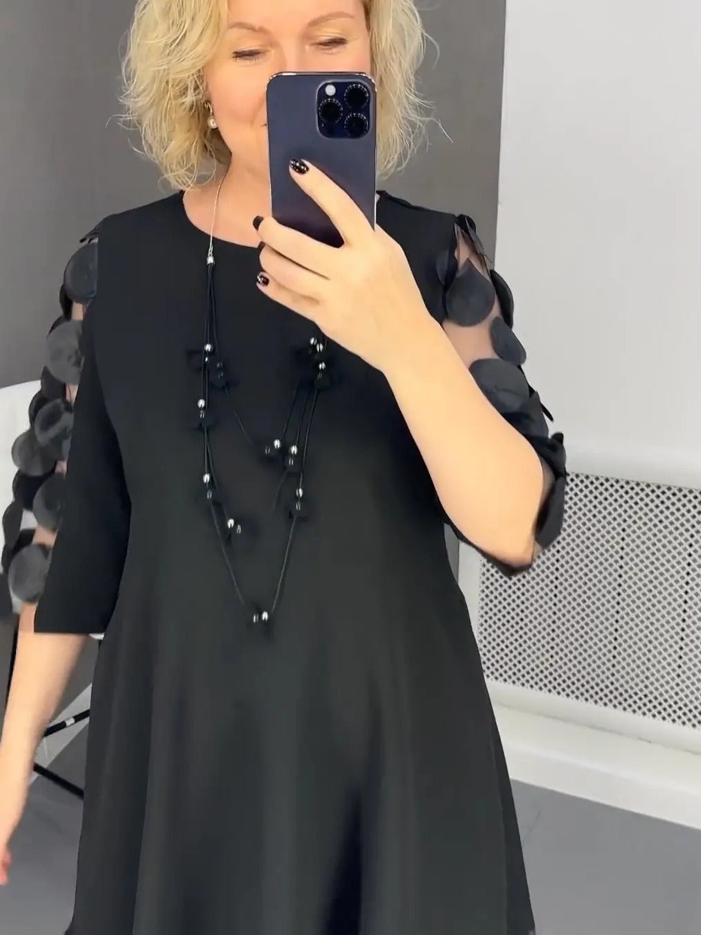 Woman wearing an elegant black dress for curvy women with sheer sleeves decorated with circular appliques