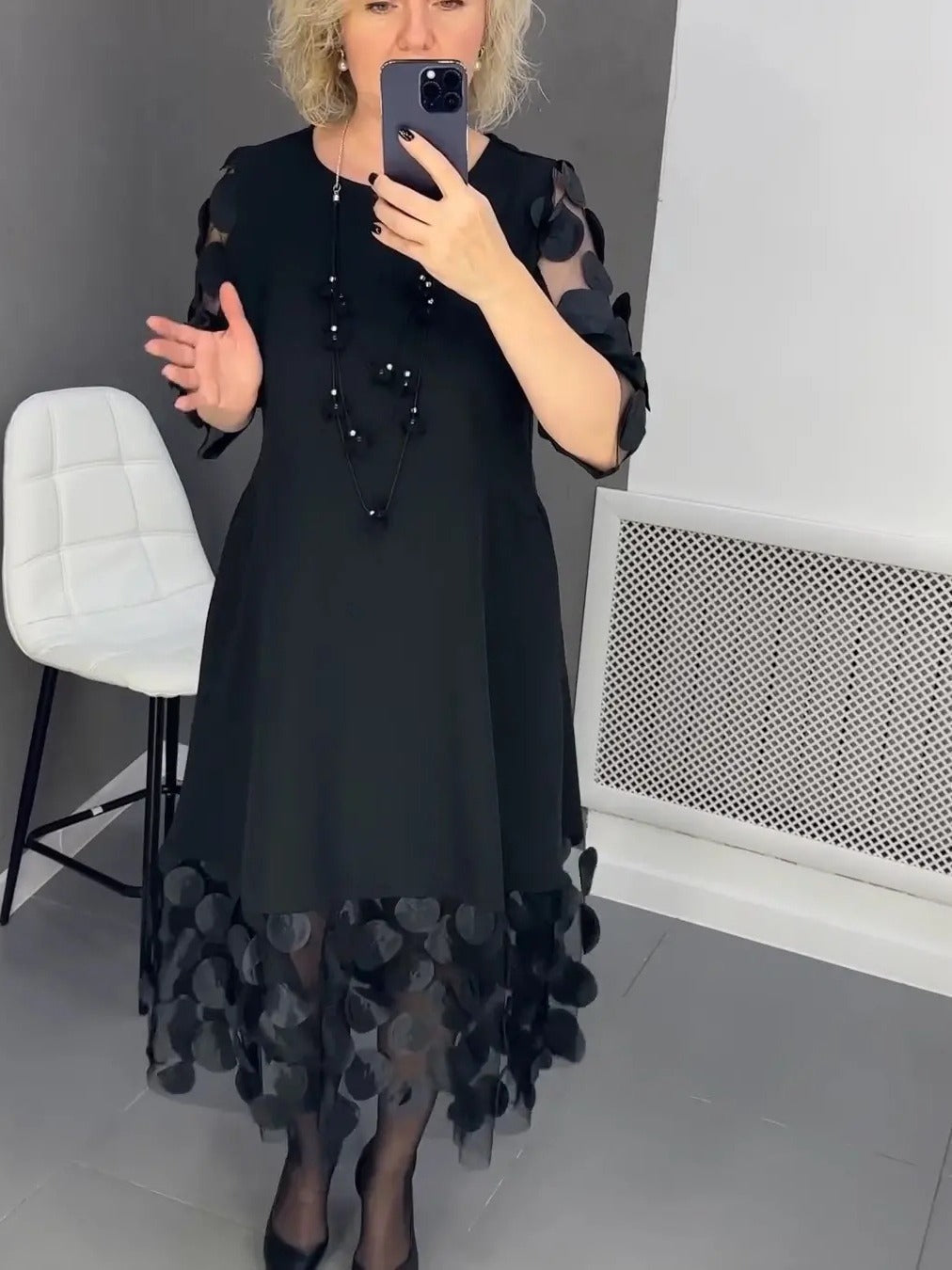 Woman wearing an elegant black dress for curvy women with sheer polka dot sleeves and hemline
