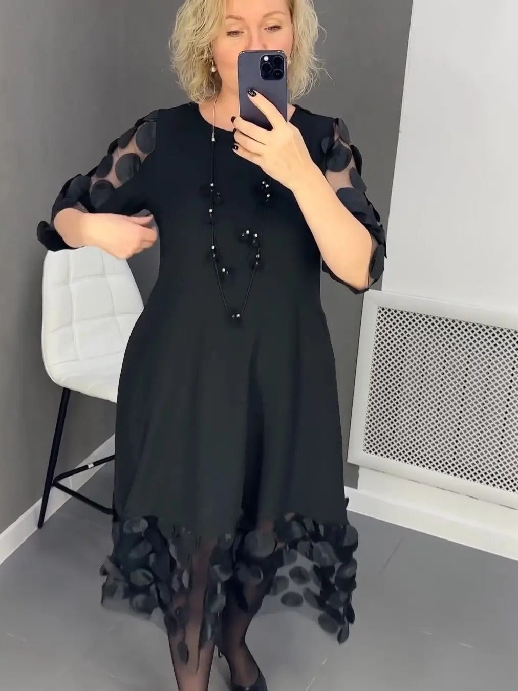 Elegant black dress for curvy women with sheer polka dot sleeves and hem detail worn by woman
