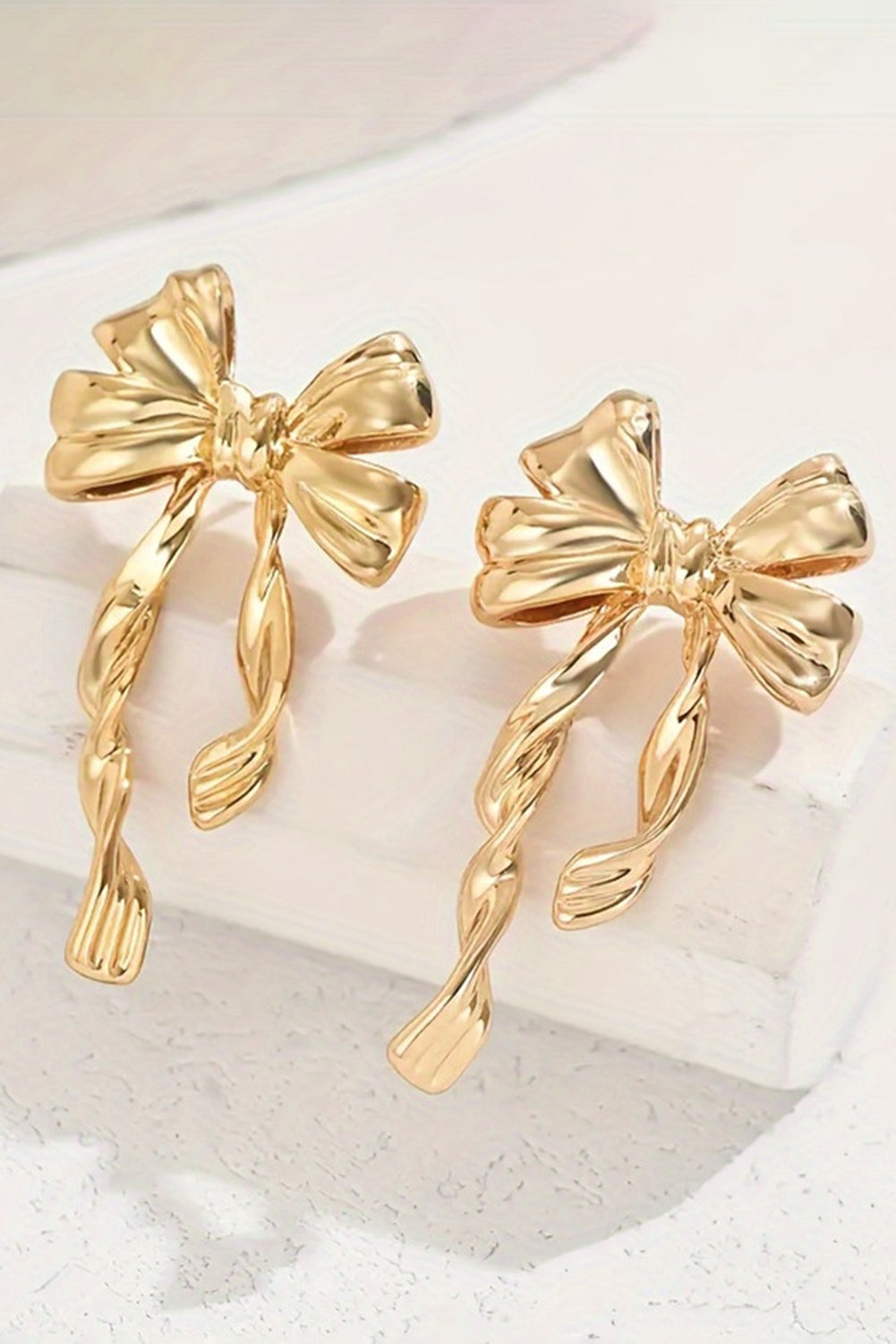 Gold bow stud earrings with twisted ribbon design in shiny metal finish