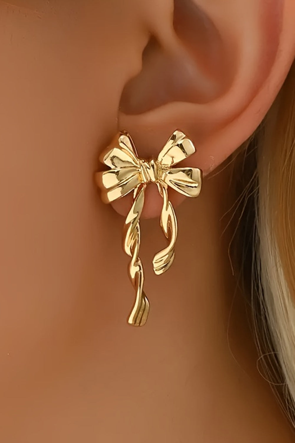 Close-up of gold bow stud earrings worn on ear with delicate ribbon design