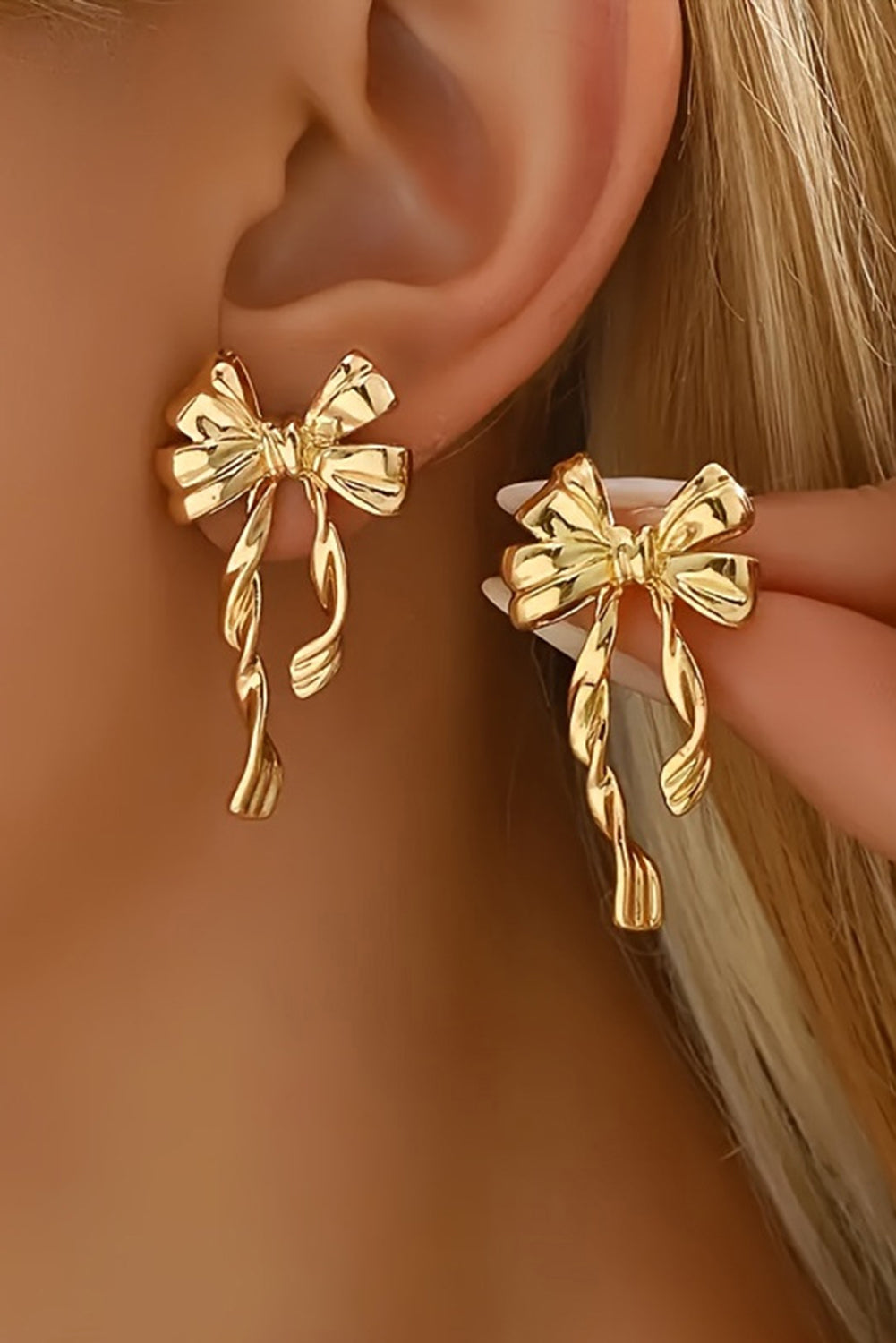 Gold bow stud earrings worn on ear and held by hand showcasing elegant bow design