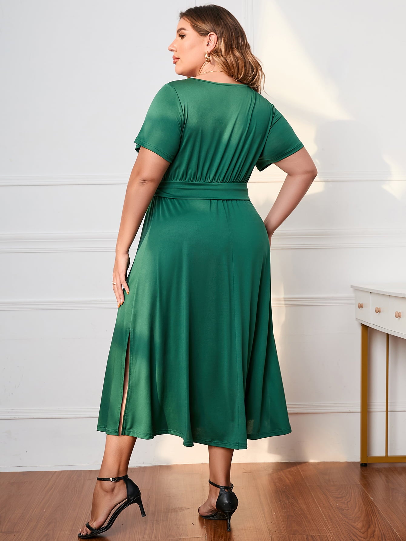Back view of green plus size short sleeve dress with waist tie and side slit paired with black heels