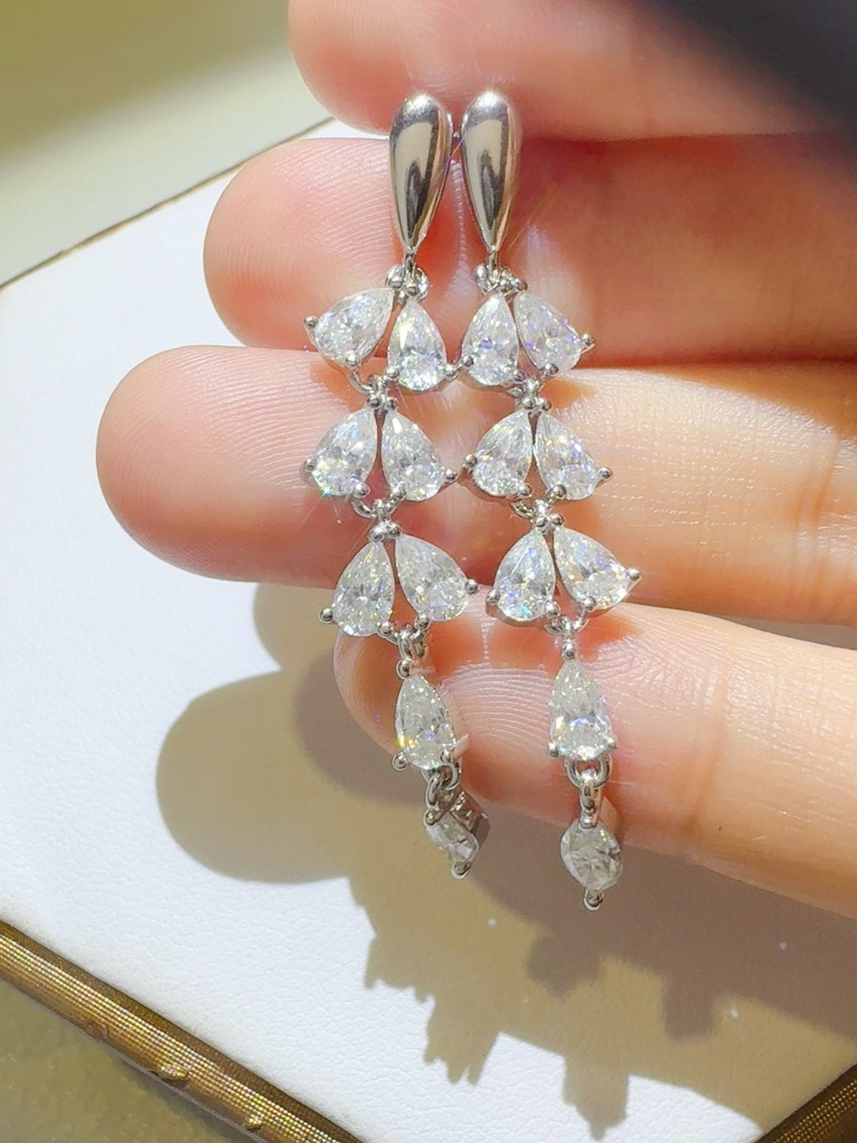 Trendsi moissanite bar earrings with multiple sparkling pear-shaped stones held between fingers