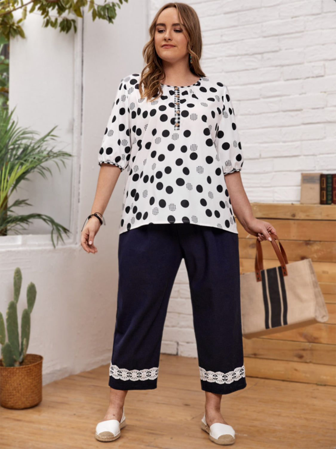 Plus size polka dot blouse with three-quarter sleeves worn by model paired with navy cropped pants