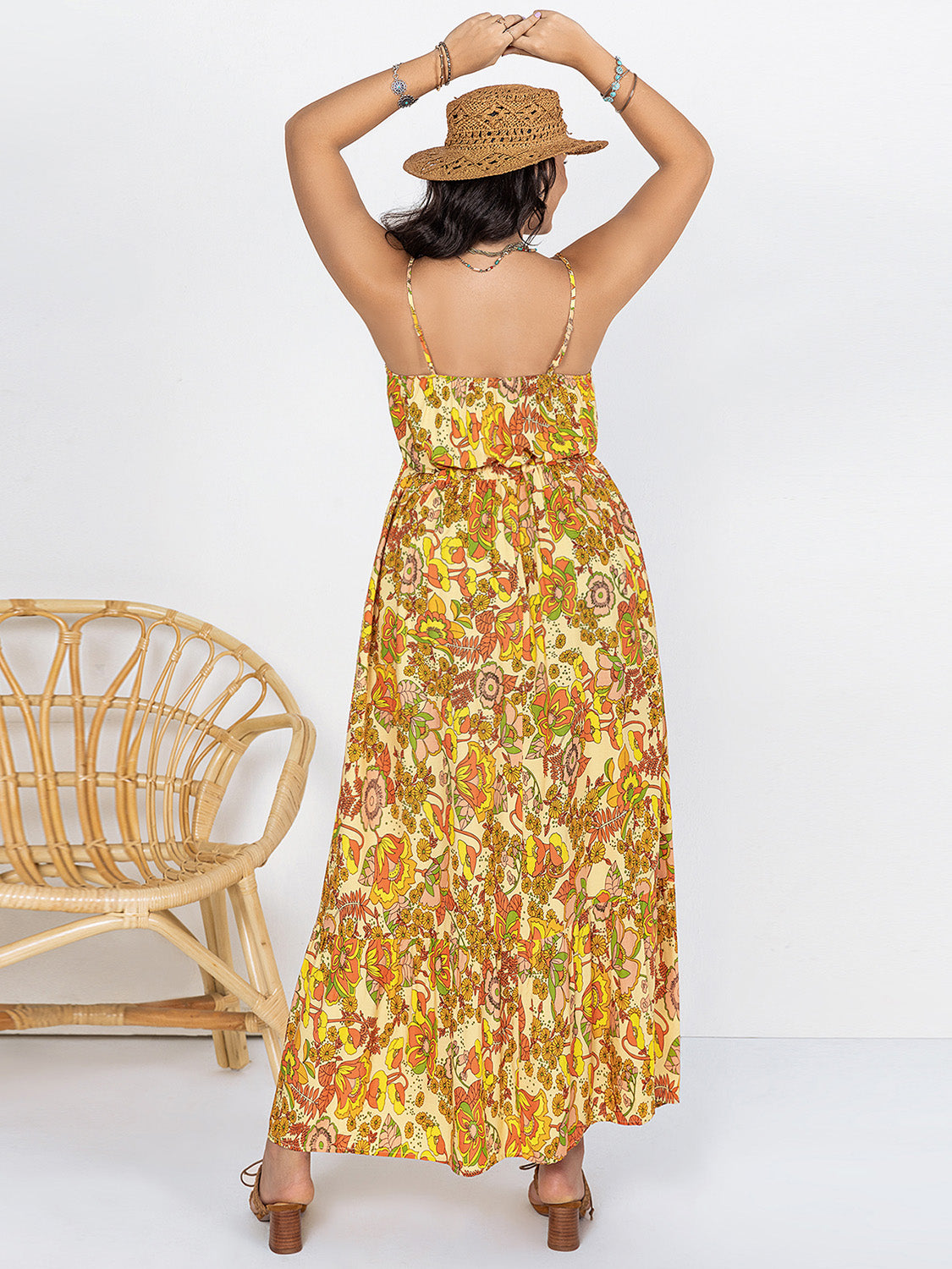 Back view of plus size printed maxi dress in yellow floral pattern worn with a straw hat and sandals