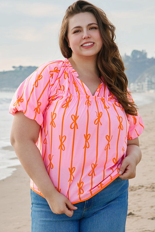 Plus size rose bowknot blouse in pink with orange bow designs worn by smiling woman at the beach