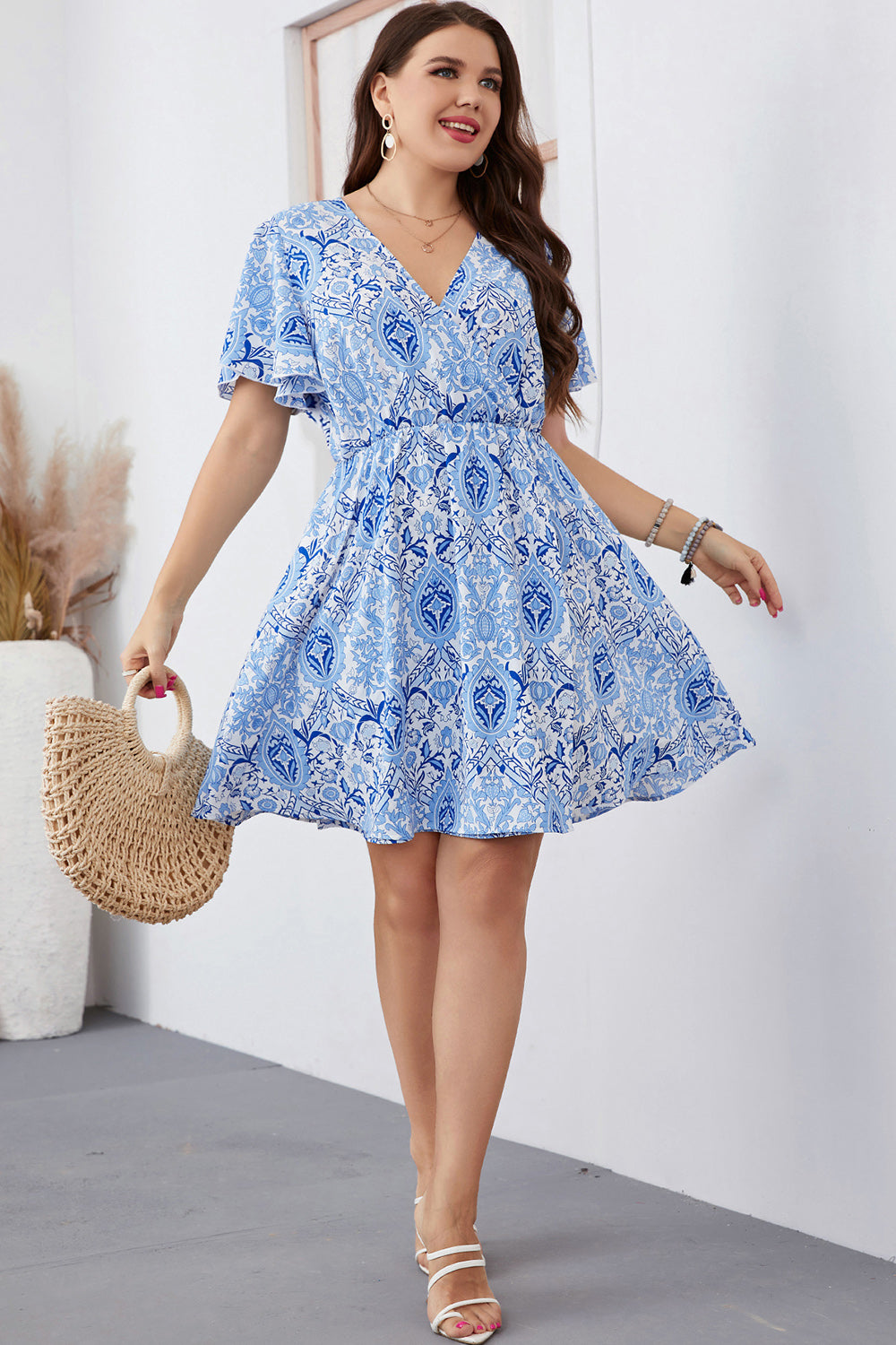 Plus size surplice neck dress in blue and white floral print with flutter sleeves and a flowy skirt
