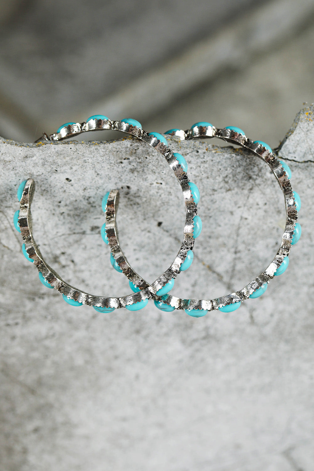 Silver hoop earrings adorned with sky blue gem hoop earrings from kjplussizefashion on a textured stone background