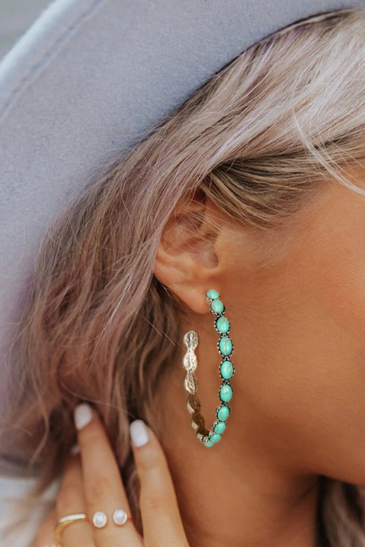 Close-up of sky blue gem hoop earrings worn by woman with blonde hair and gray hat