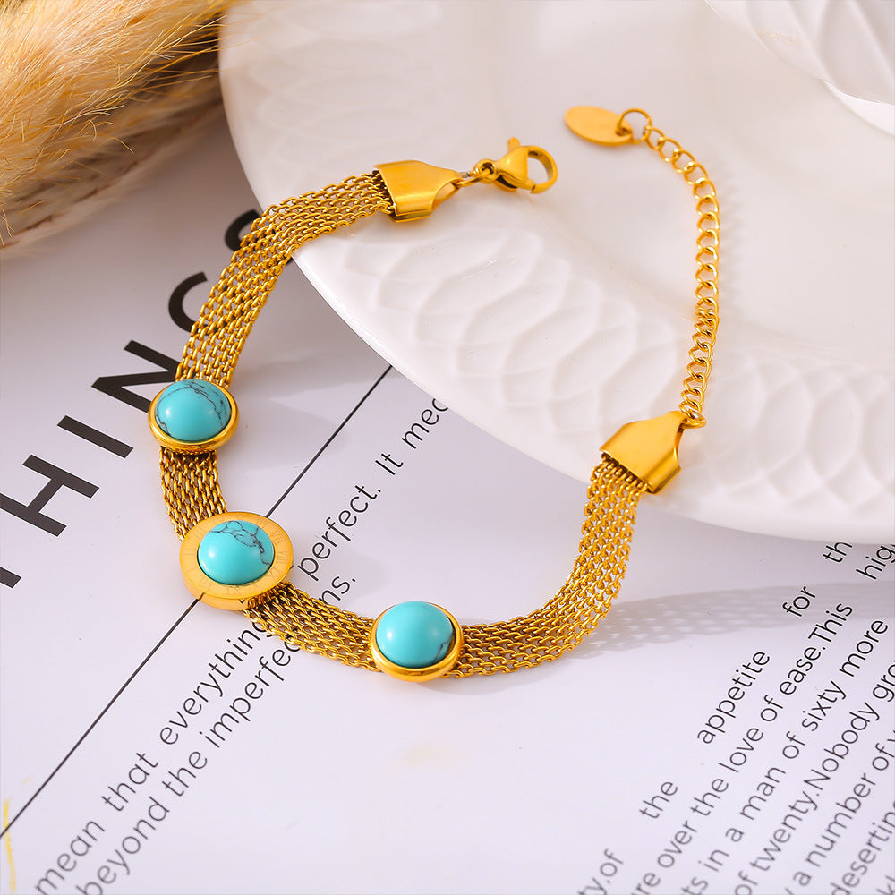 Turquoise titanium steel bracelet with gold mesh chain and round turquoise stones on a white plate