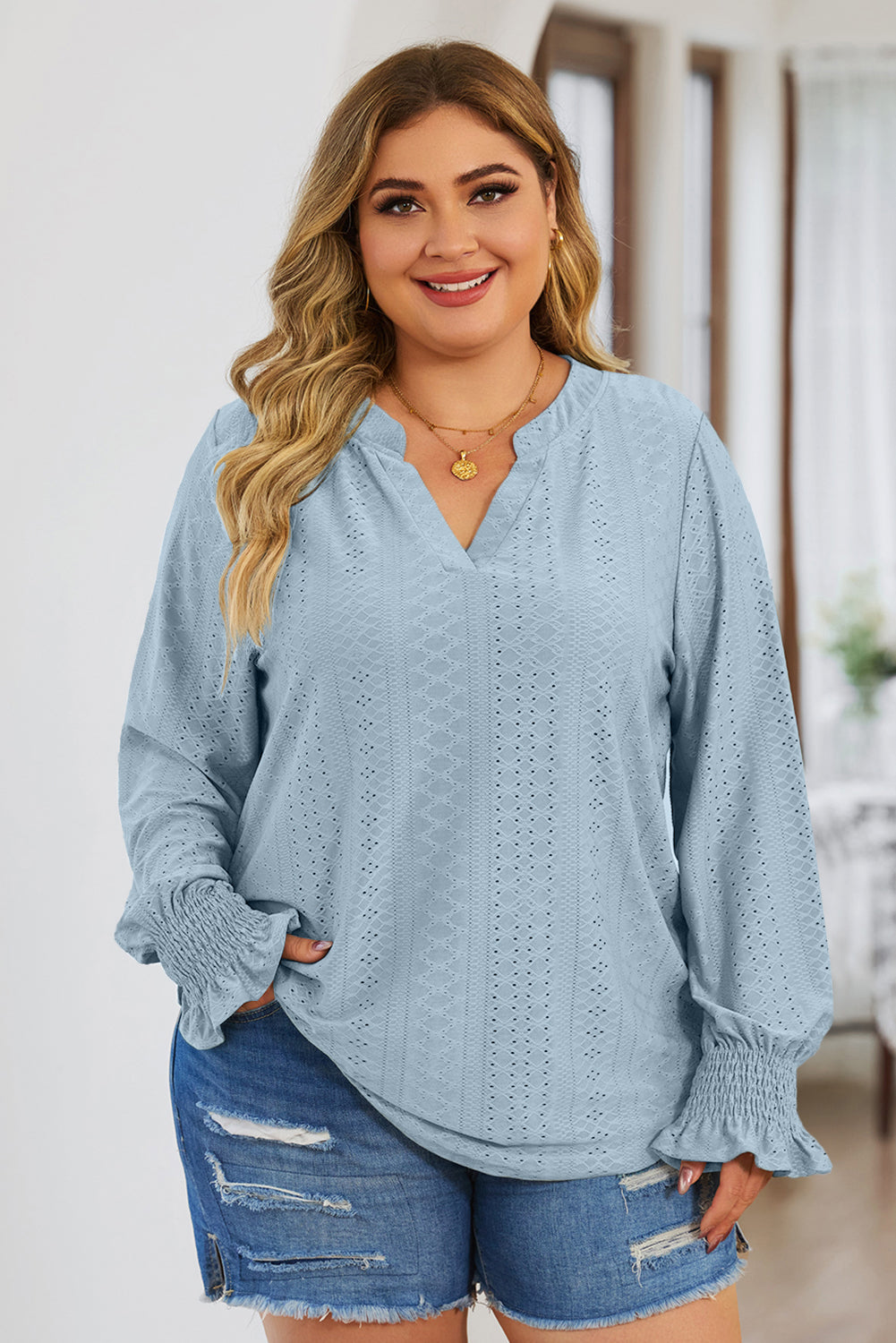 Plus size trendy blouse for women in light blue with long sleeves and eyelet details worn by smiling woman
